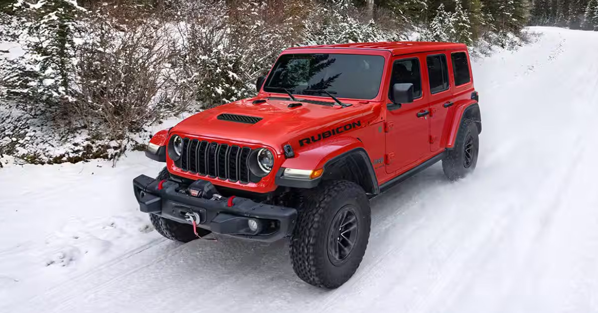 Red Jeep Wrangler Rubicon driving through a snowy forest trail with off-road tires and rugged winter capability.